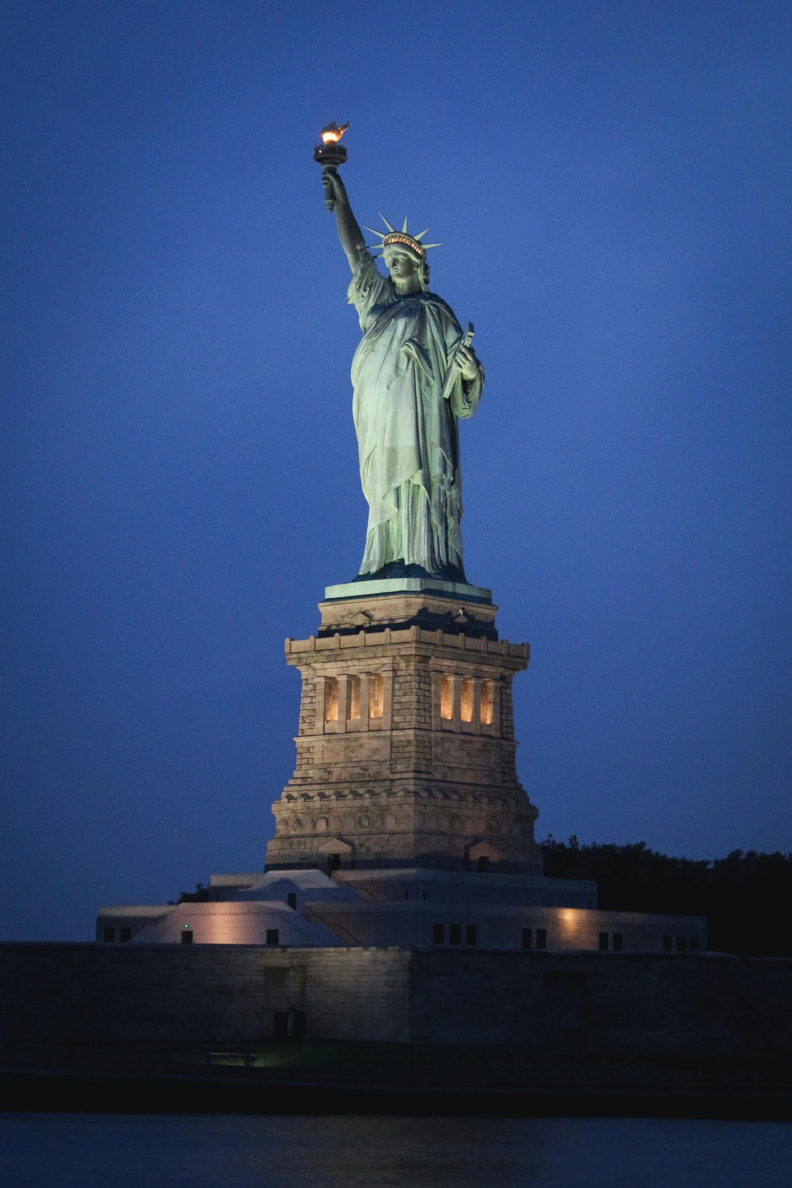 the statue of liberty is lit up at night, a statue, by Greg Rutkowski, viewed from the side, at dusk