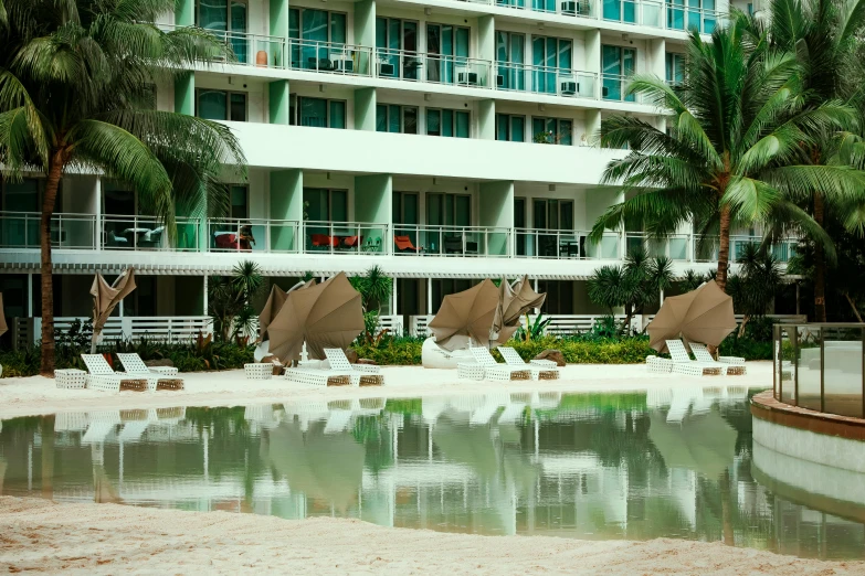 a pool with chairs and umbrellas in front of a building, by Carey Morris, pexels contest winner, sea - green and white clothes, coconuts, public art, full building