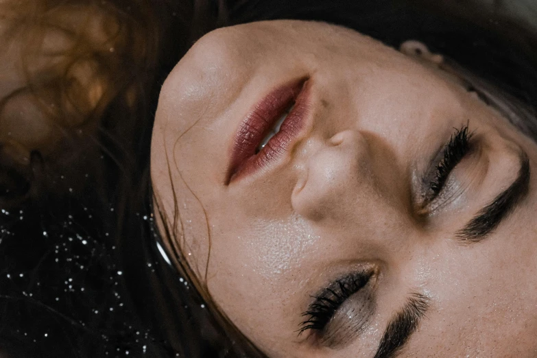 a woman laying down with her eyes closed, inspired by Elsa Bleda, trending on pexels, hyperrealism, wet lips, film still from horror movie, dark glitter makeup, a redheaded young woman