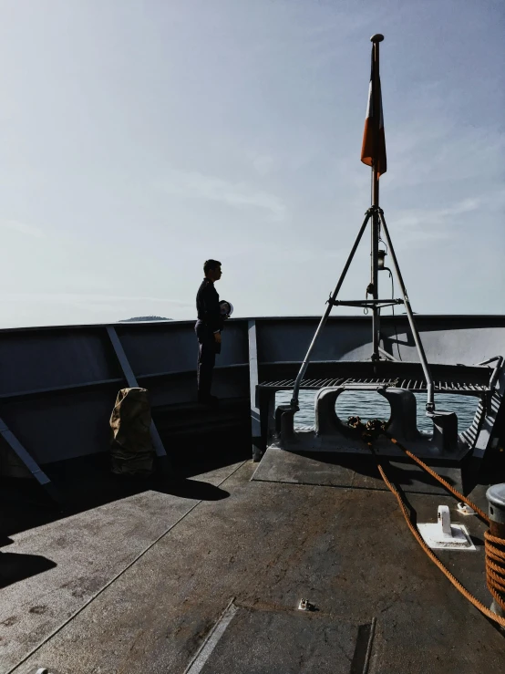 a man standing on top of a boat next to the ocean, command presence, photo taken from behind, on the deck of a ship, on a landing pad