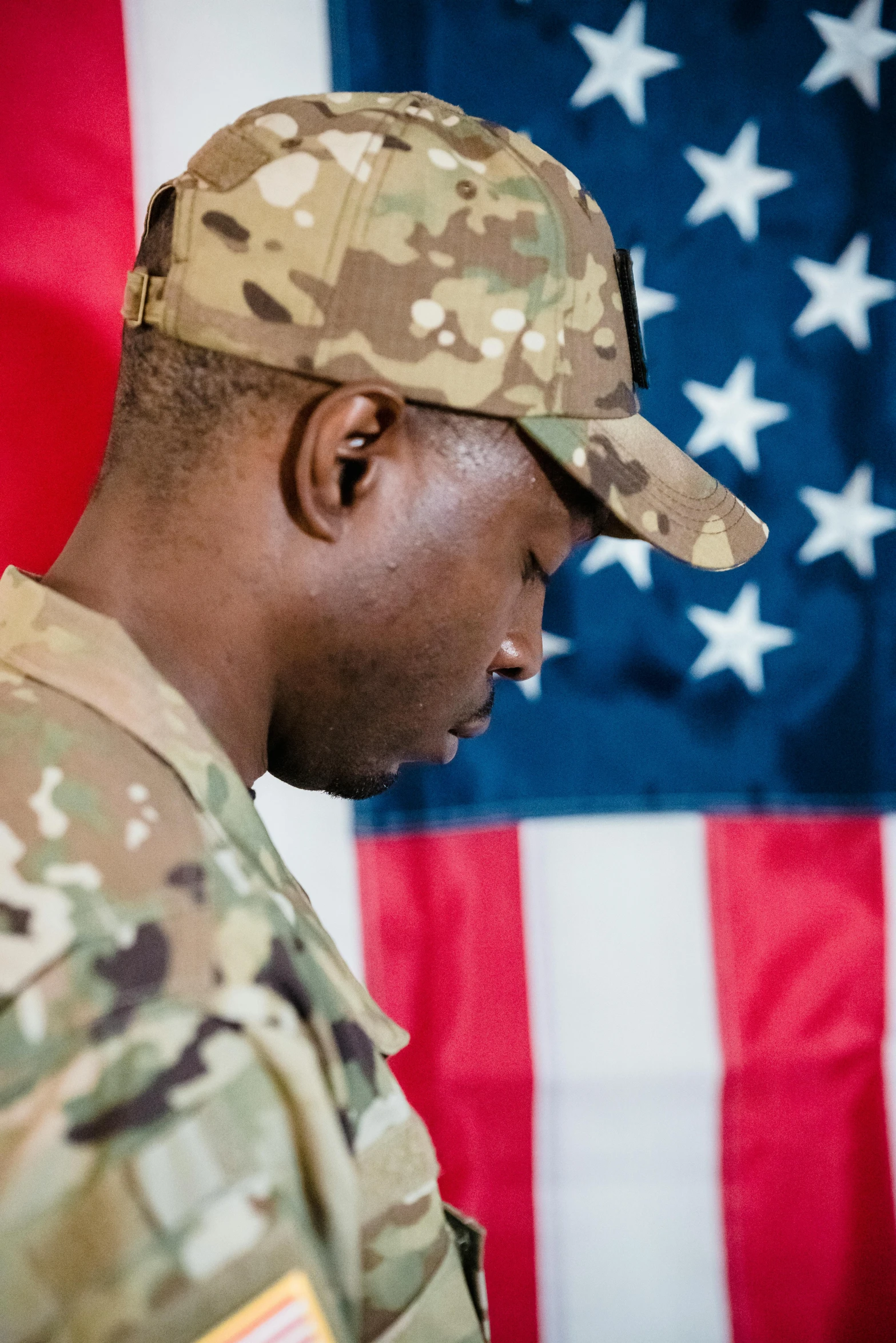 a man in uniform standing in front of an american flag, a picture, shutterstock, digital art, sorrow, ( ( dark skin ) ), multicam (camo), heartbroken