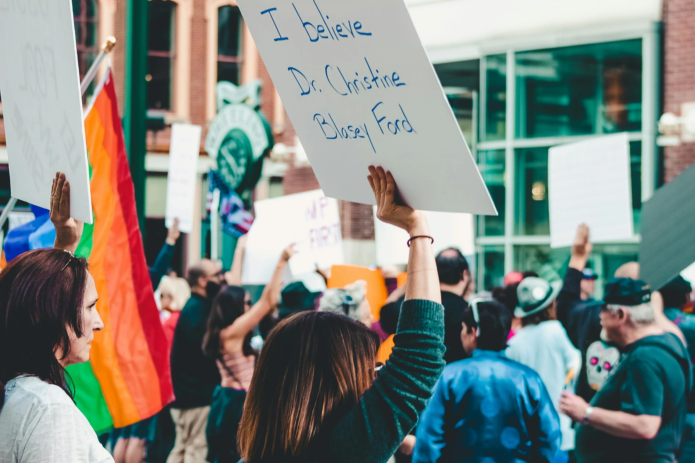 a woman holding a sign in front of a crowd of people, by Julia Pishtar, pexels, institutional critique, lgbt, background image