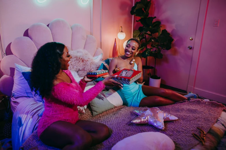 a couple of women sitting on top of a bed, an album cover, trending on pexels, happening, purple and pink and blue neons, sitting in a lounge, presents, laughing