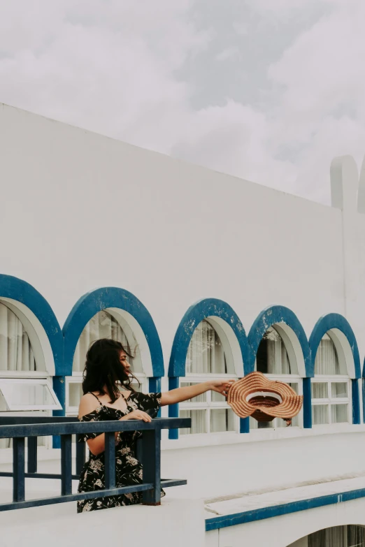 a woman standing on a balcony holding a guitar, by Olivia Peguero, pexels contest winner, arabesque, blue! and white colors, curving geometric arches, wearing sombrero, white building