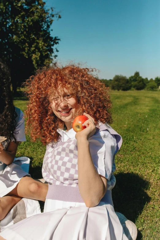 a couple of women sitting on top of a lush green field, an album cover, inspired by Kaja Foglio, trending on pexels, renaissance, holding an apple, curly red hair, dressed as schoolgirl, eating outside