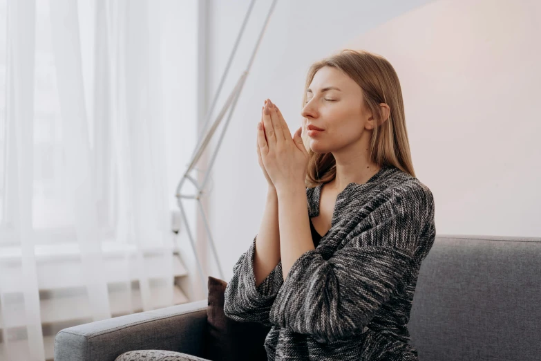 a woman sitting on a couch with her eyes closed, trending on pexels, hurufiyya, praying posture, max dennison, profile image, hands shielding face