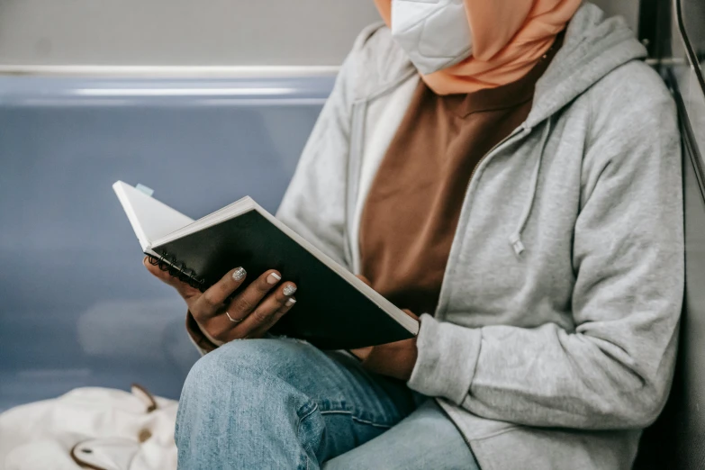 a woman sitting on a train reading a book, face covered, riyahd cassiem, without text, grey