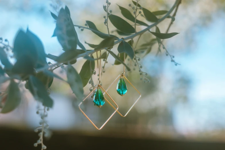 a pair of earrings hanging from a tree branch, inspired by Elsa Bleda, pexels contest winner, crystal cubism, green square, gold, brandon woelfel, miniature product photo