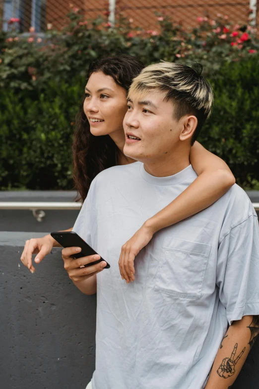 a man and a woman standing next to each other, trending on pexels, happening, half asian, phone in hand, non binary model, grey