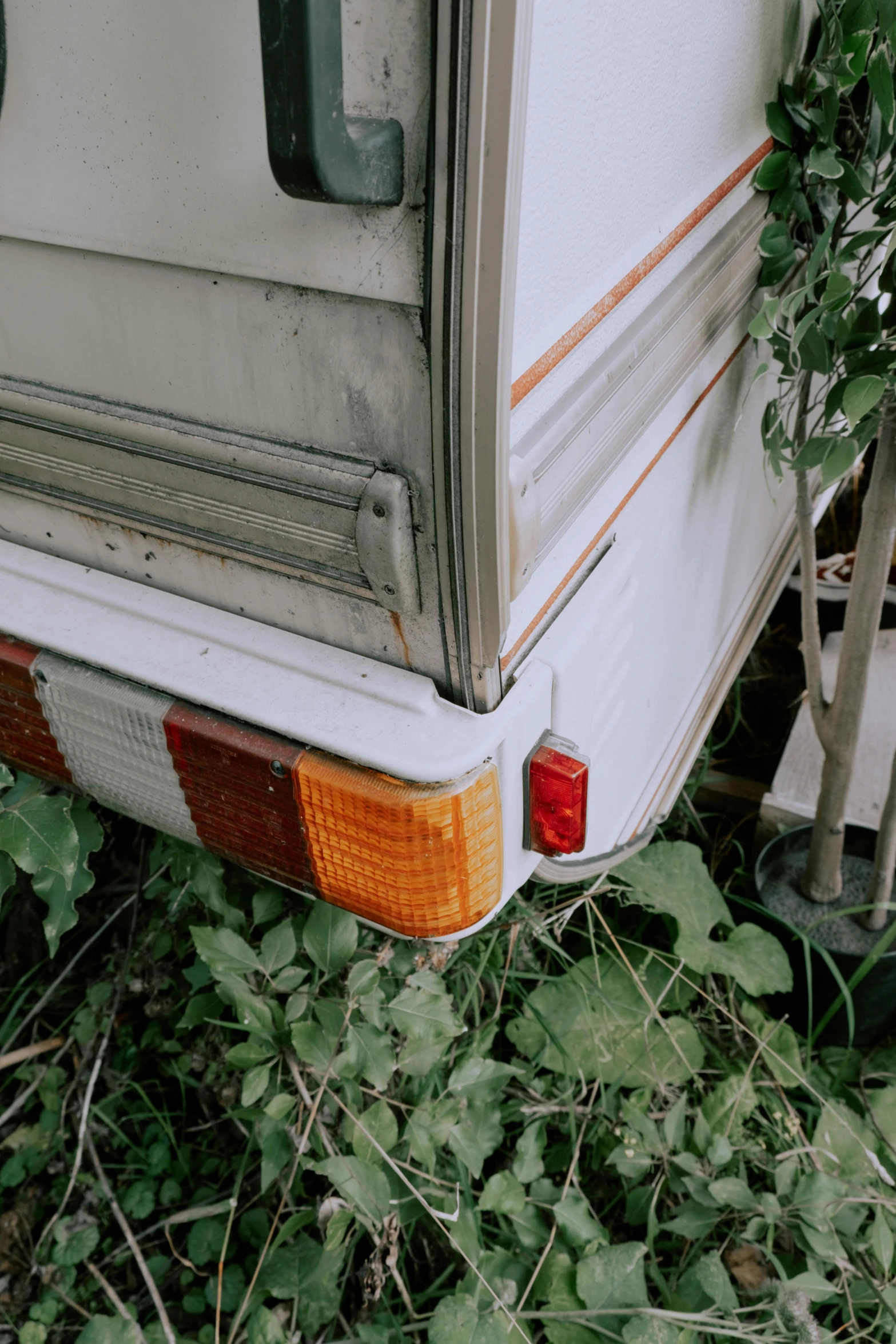 an old camper parked on the side of the road, by Elsa Bleda, unsplash, tail lights, overgrown with weeds, low quality photo, white plastic