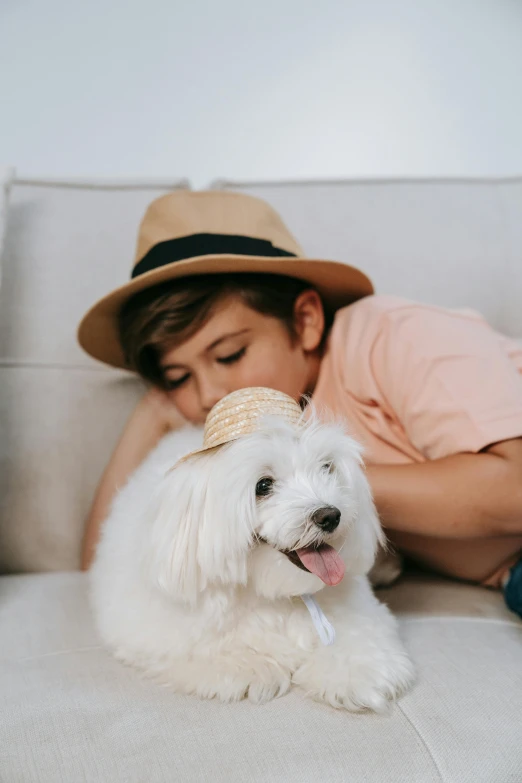 a little boy laying on a couch with a white dog, pexels contest winner, white straw flat brimmed hat, profile image, male teenager, fluffy