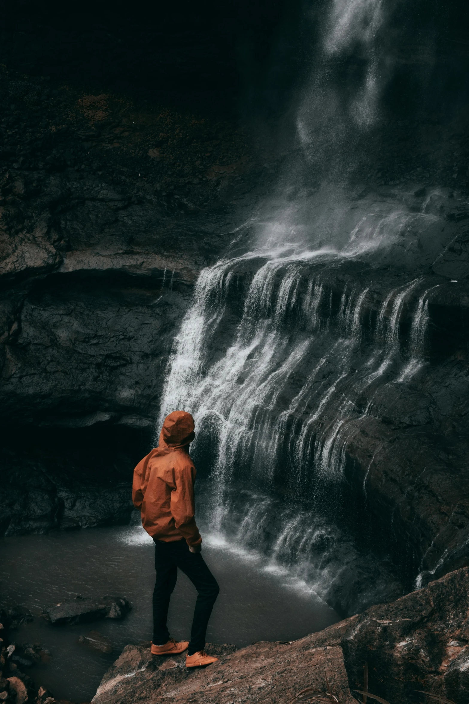 a person standing in front of a waterfall, by Daniel Seghers, unsplash contest winner, low key, vsco film grain, rainy environment, cavern