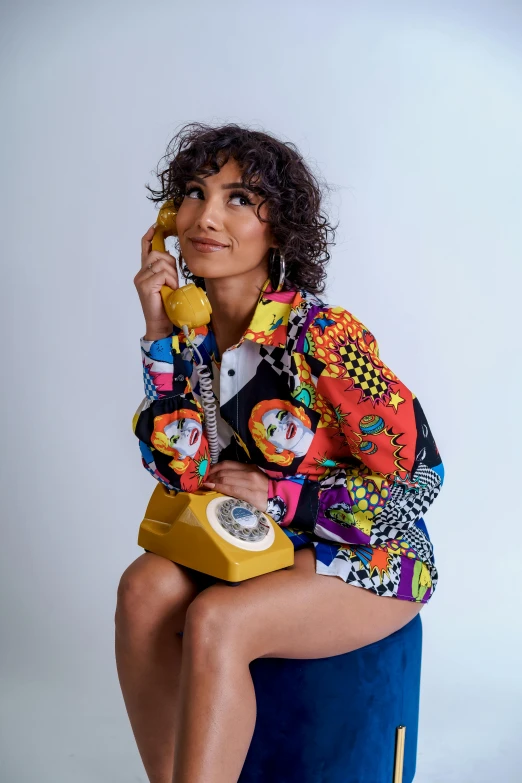 a woman sitting on a stool talking on a phone, trending on pexels, pop art, patterned clothing, ashteroth, looking towards camera, she wears a jacket