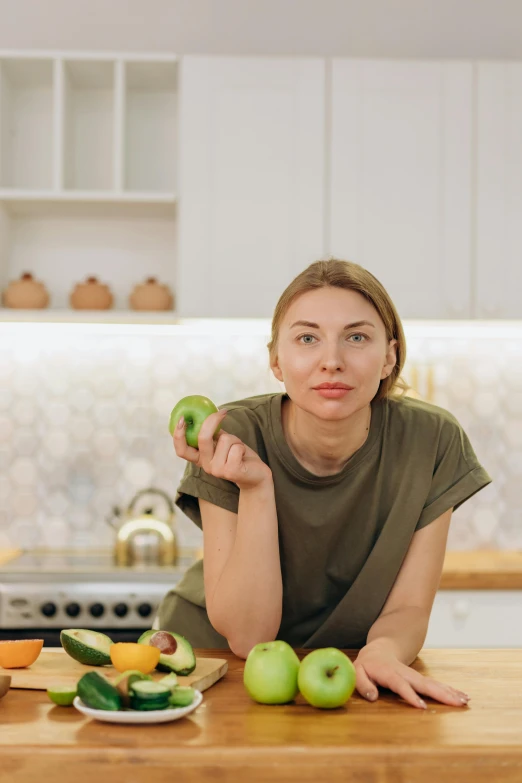 a woman sitting at a kitchen table holding an apple, by Julia Pishtar, pexels contest winner, cucumber, angelina stroganova, kiwi, low quality photo