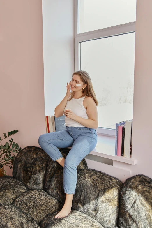 a woman sitting on top of a couch next to a window, by Julia Pishtar, wearing jeans, nordic pastel colors, thicc, woman / cat hybrid