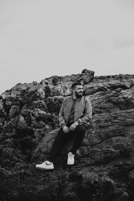 a black and white photo of a man sitting on a rock, drake, artem, profile image, single subject