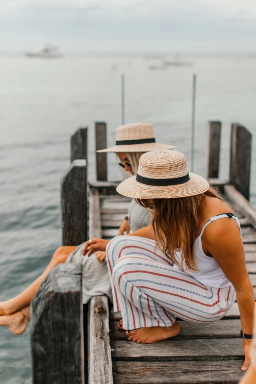 a couple of women sitting on top of a wooden pier, pexels contest winner, white straw flat brimmed hat, manly, thoughtful, striped