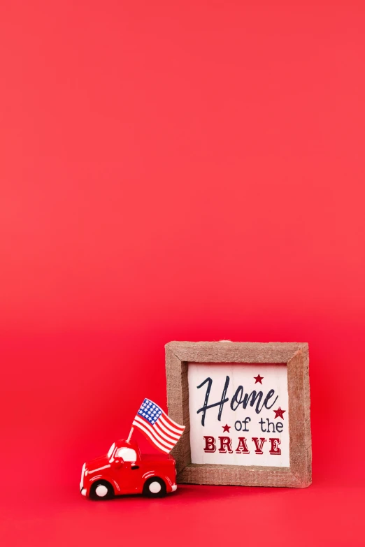 a toy car next to a sign that says home of the brave, a picture, pexels, red white background, made of bronze, uniform background, portrait n - 9