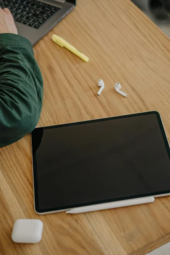a laptop computer sitting on top of a wooden desk, applepencil, earbuds, using a magical tablet, tiny person watching