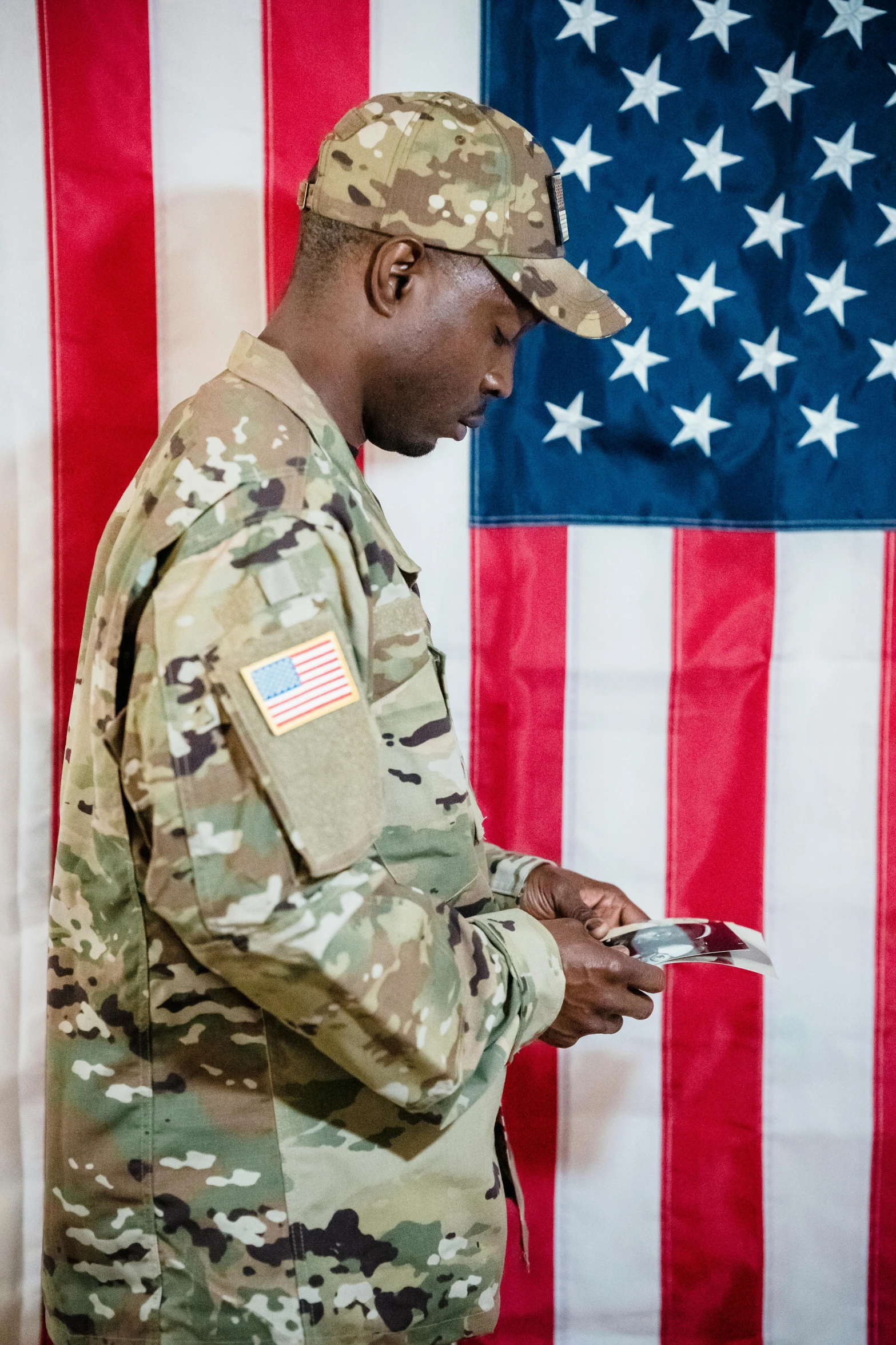 a man in uniform standing in front of an american flag, looking at his phone, camo, inspect in inventory image, religious