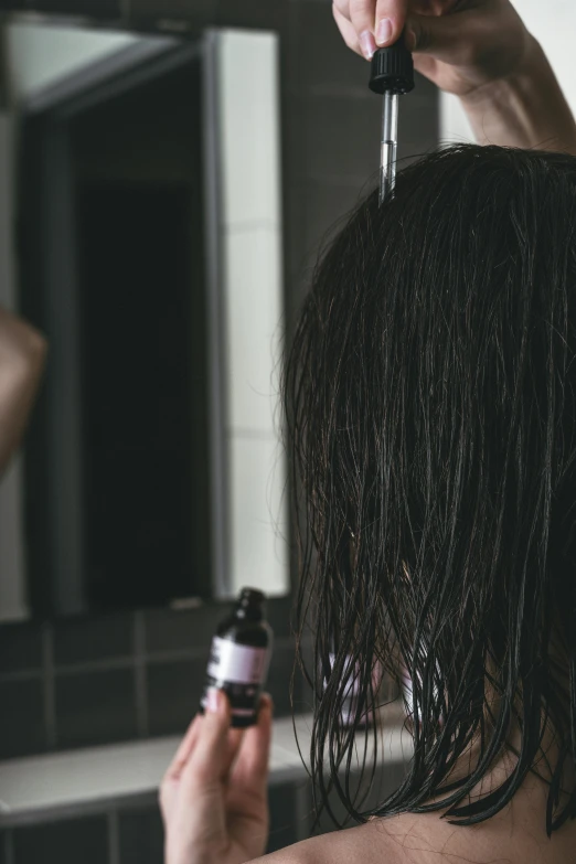 a woman combing her hair in front of a mirror, pexels contest winner, droplets flow down the bottle, dark brown hair, bedhead, back towards camera