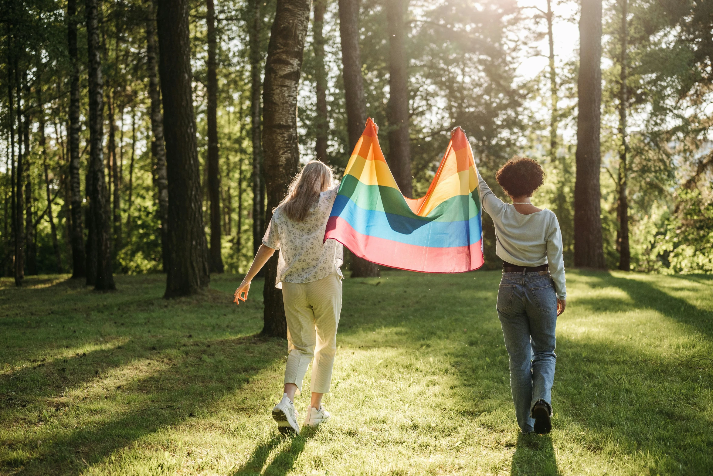 a couple of people that are holding a rainbow flag, a photo, shutterstock, girl walking in forest, cottagecore, green flag, lesbian