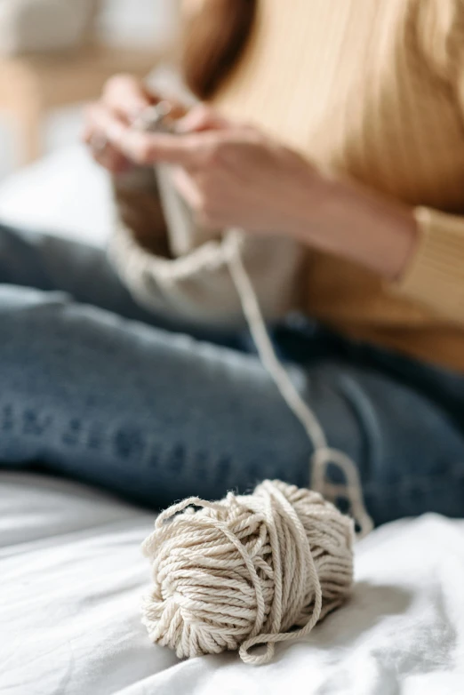 a woman sitting on a bed with a ball of yarn, trending on pexels, wearing a white sweater, creating a soft, game, denim