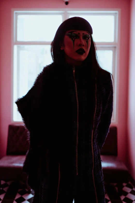 a woman standing in front of a window in a room, an album cover, unsplash, transgressive art, wearing goth makeup, asian women, she wears a jacket, press photos