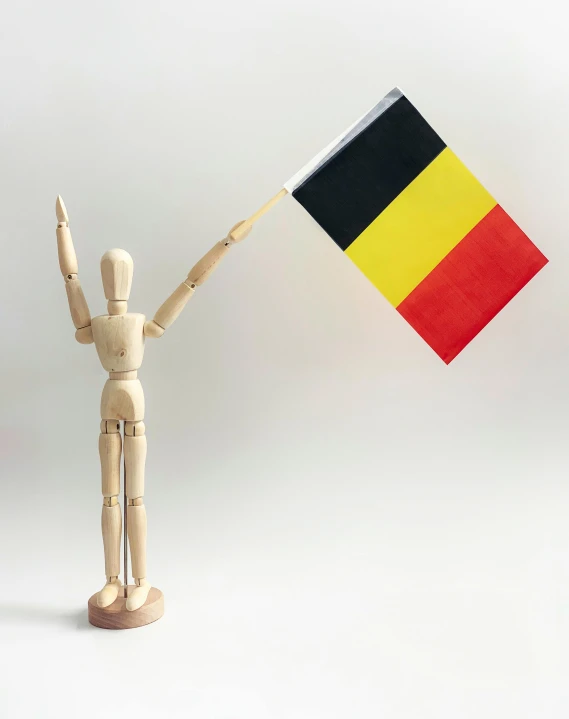 a wooden mannequin holding a black, yellow and red flag, inspired by Jan Verkolje, hands in air, belgium, non-binary, rectangle