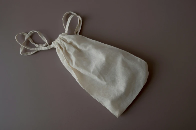 a white bag sitting on top of a table, by Helen Stevenson, unsplash, mingei, on a gray background, ecru cloth, halter top, bedhead