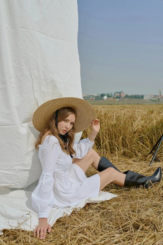 a woman sitting on top of a pile of hay, an album cover, by Wen Zhenheng, unsplash, renaissance, white straw flat brimmed hat, white blouse and gothic boots, 2 4 year old female model, ulzzang