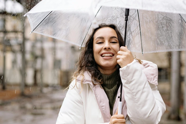 a woman holding an umbrella in the rain, trending on unsplash, happening, smiling young woman, wearing a white winter coat, thumbnail, background image