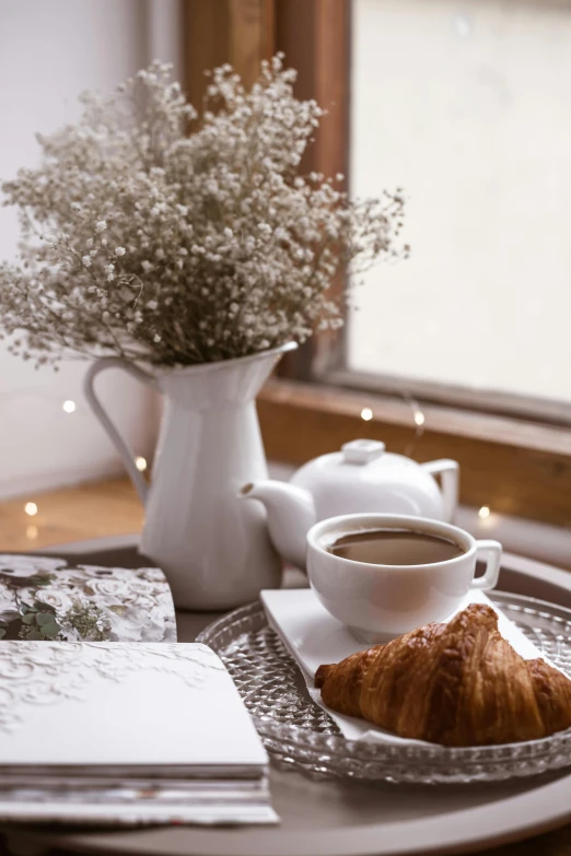 a plate topped with a croissant next to a cup of coffee, a still life, pexels contest winner, romanticism, gypsophila, natural light in room, winter setting, profile image