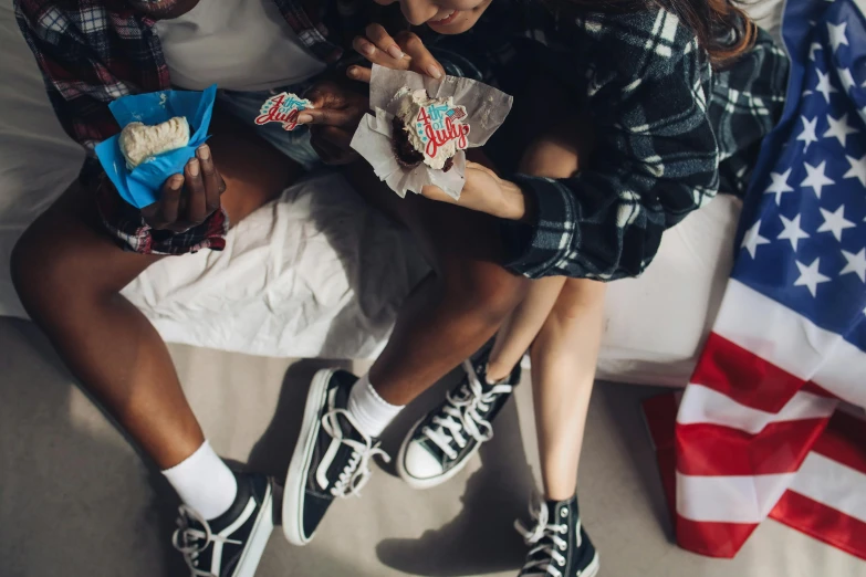 a couple of people sitting on top of a bed, by Julia Pishtar, trending on pexels, coke and chips on table, wearing red converse shoes, teenage jughead jones, snacks