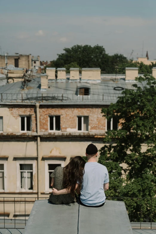 a man and a woman sitting on top of a building, by Adam Marczyński, seen from afar, russian city, trees in background, facing away