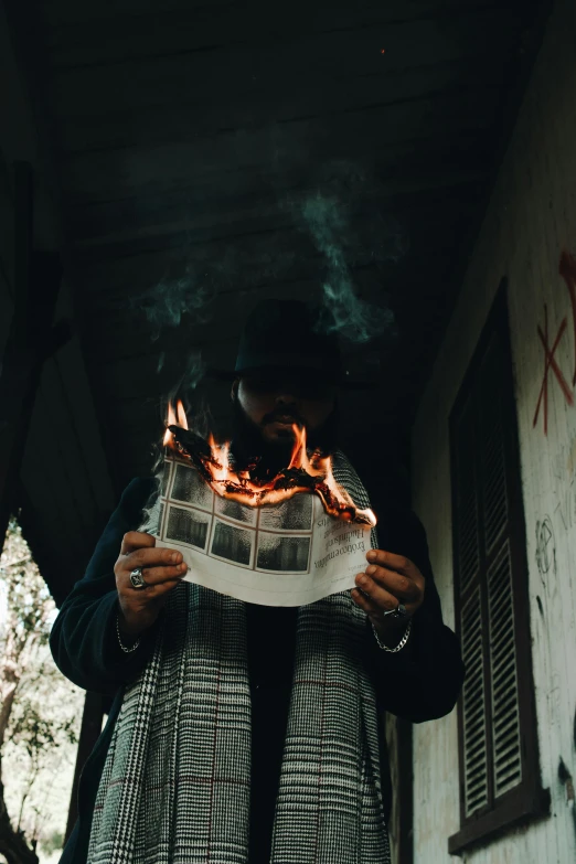 a person standing on a porch holding a newspaper, an album cover, pexels contest winner, graffiti, all face covered with a fire, instagram picture, burning overgrowth, xenophobia
