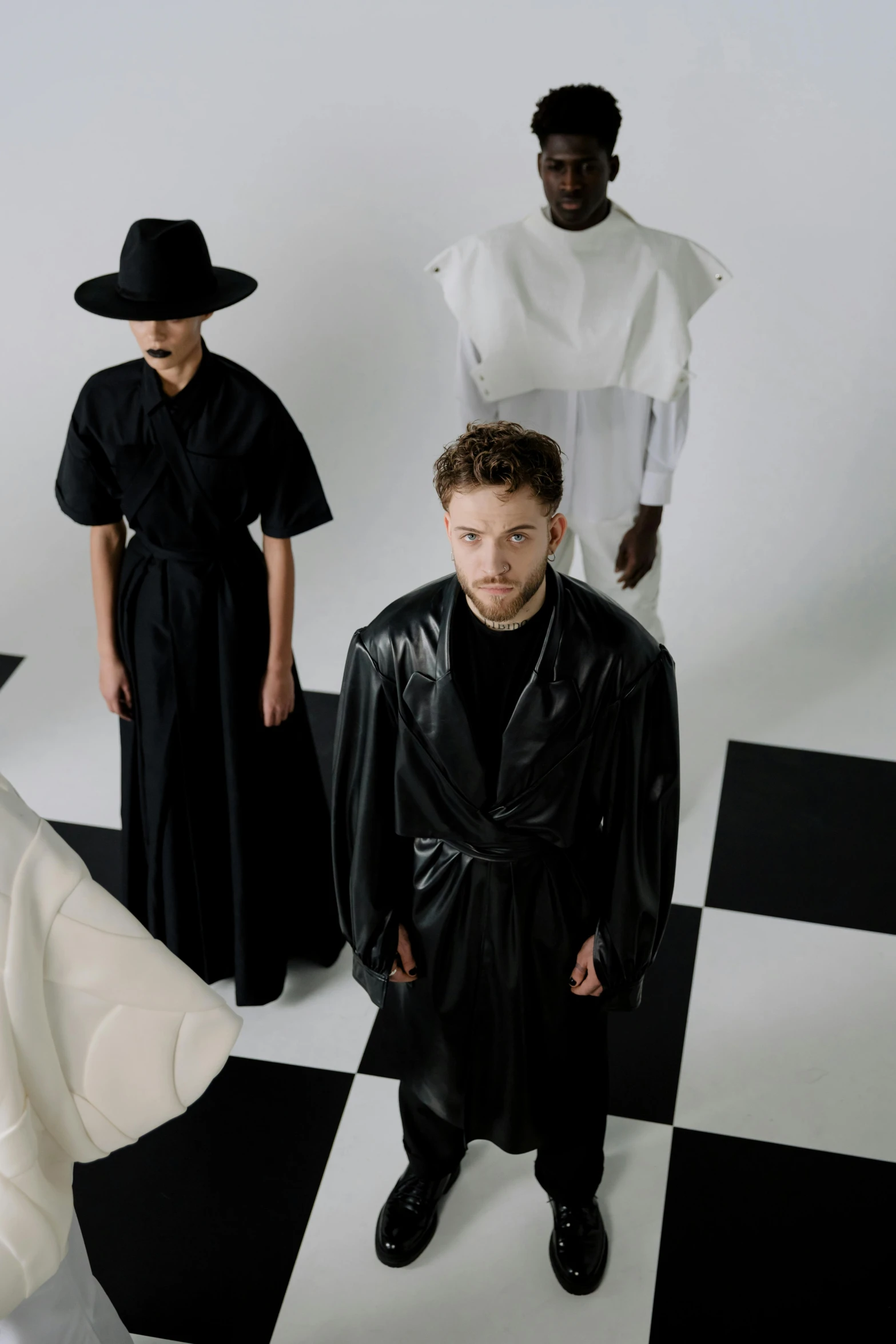 a group of people standing next to each other on a checkered floor, inspired by Jonas De Ro, trending on unsplash, bauhaus, wearing black robes, yohji yamamoto, dressed like a cleric, looking across the shoulder