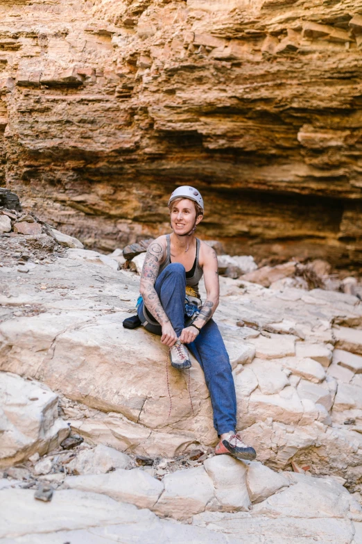 a woman sitting on a rock in a canyon, a portrait, featured on reddit, non-binary, climbing, wearing overalls, in the australian outback