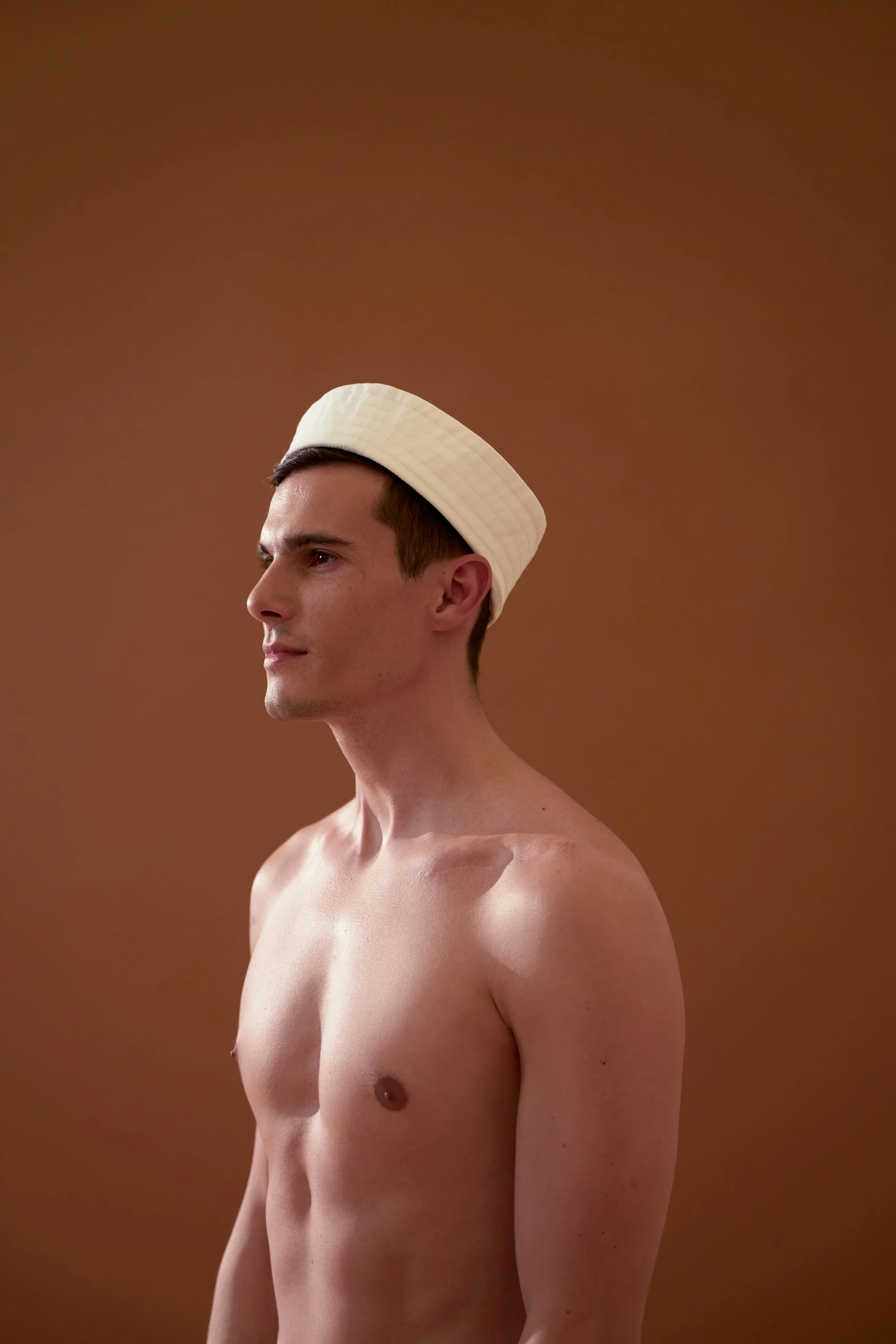 a shirtless man standing in front of a brown wall, by Nathalie Rattner, conceptual art, wearing a white bathing cap, beautiful androgynous prince, photographed for reuters, muslim