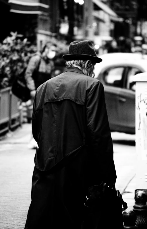 a black and white photo of a man walking down the street, unsplash, black stetson and coat, facing away, old man, male character