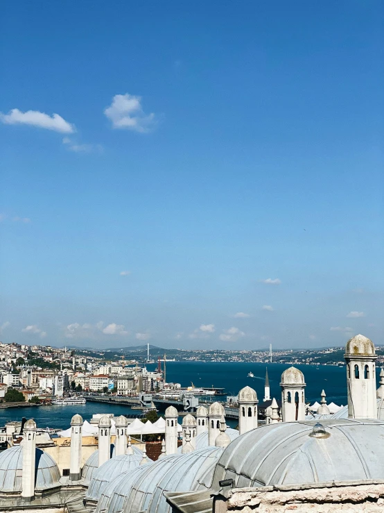 a clock tower on top of a building next to a body of water, with great domes and arches, bird's eye view of a city, light blue clear sky, mixture turkish and russian