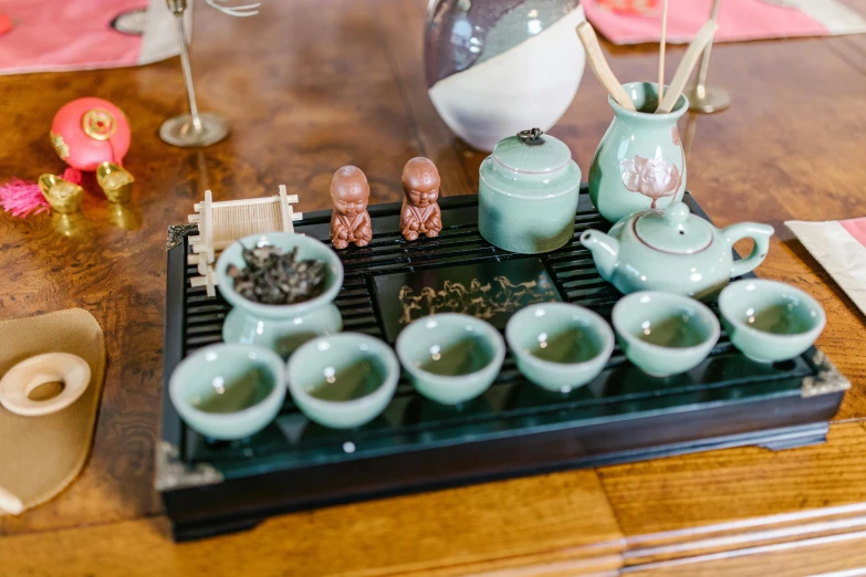 a tea set sitting on top of a wooden table, inspired by Xuande Emperor, trending on unsplash, mingei, sea green color theme, square, taoist temples and monks, tiny statue on display