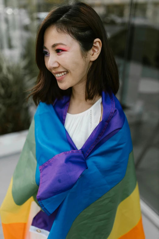 a woman wrapped in a rainbow colored blanket, inspired by Okuda Gensō, unsplash, young asian woman, draped in purple and gold silk, casually dressed, detail shot