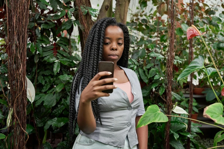 a woman standing in a garden looking at her cell phone, inspired by Chinwe Chukwuogo-Roy, pexels contest winner, realism, mirror selfie, black teenage girl, woman with braided brown hair, biophilia mood