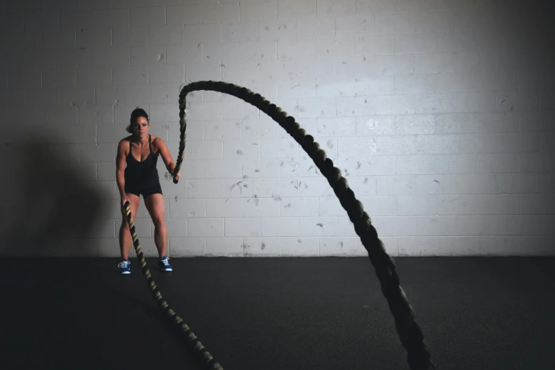 a woman holding a rope in a gym, by Jessie Algie, pexels contest winner, rubber hose style, fast movement, thumbnail, large chain