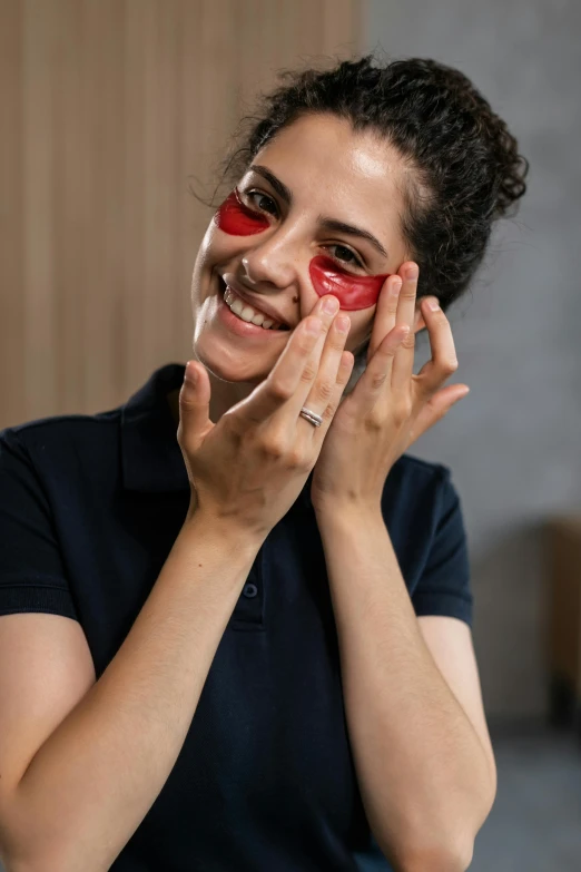 a woman with a pair of red eye patches on her face, by Julia Pishtar, professional product photo, smiles, making of, middle eastern skin