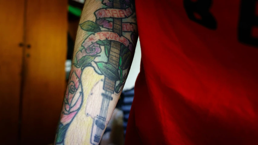 a man with a tattoo on his arm, by Alejandro Obregón, pexels, colored in, holding electric guitar, rose tattoo, taken in the late 2010s