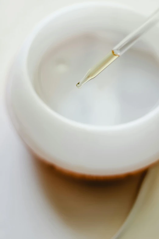 a close up of a spoon in a bowl of liquid, unsplash, white wax, promo image, needles, white and gold color scheme