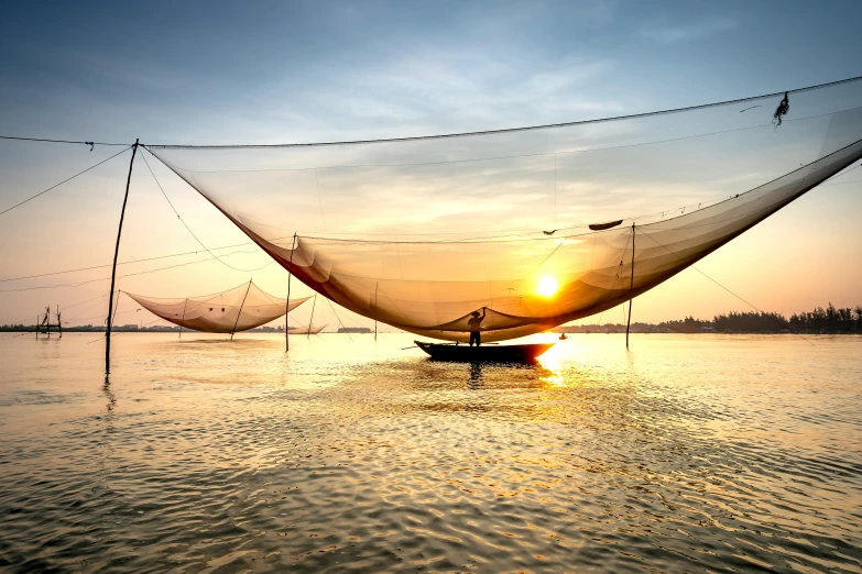 a man standing on top of a boat in a body of water, by Eglon van der Neer, pexels contest winner, silk tarps hanging, asian sun, nets, warmly lit