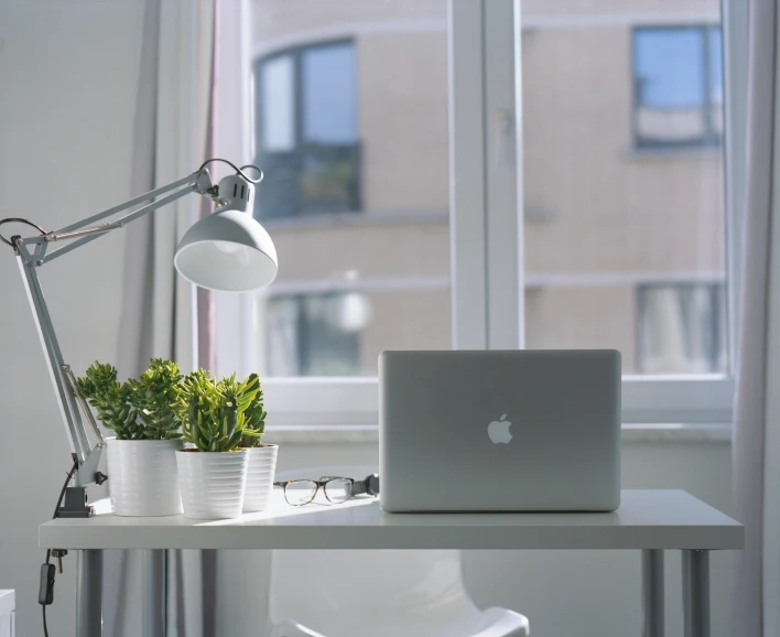 a laptop computer sitting on top of a white desk, unsplash, light and space, small plants on the window sill, single light, with apple, small and cosy student bedroom